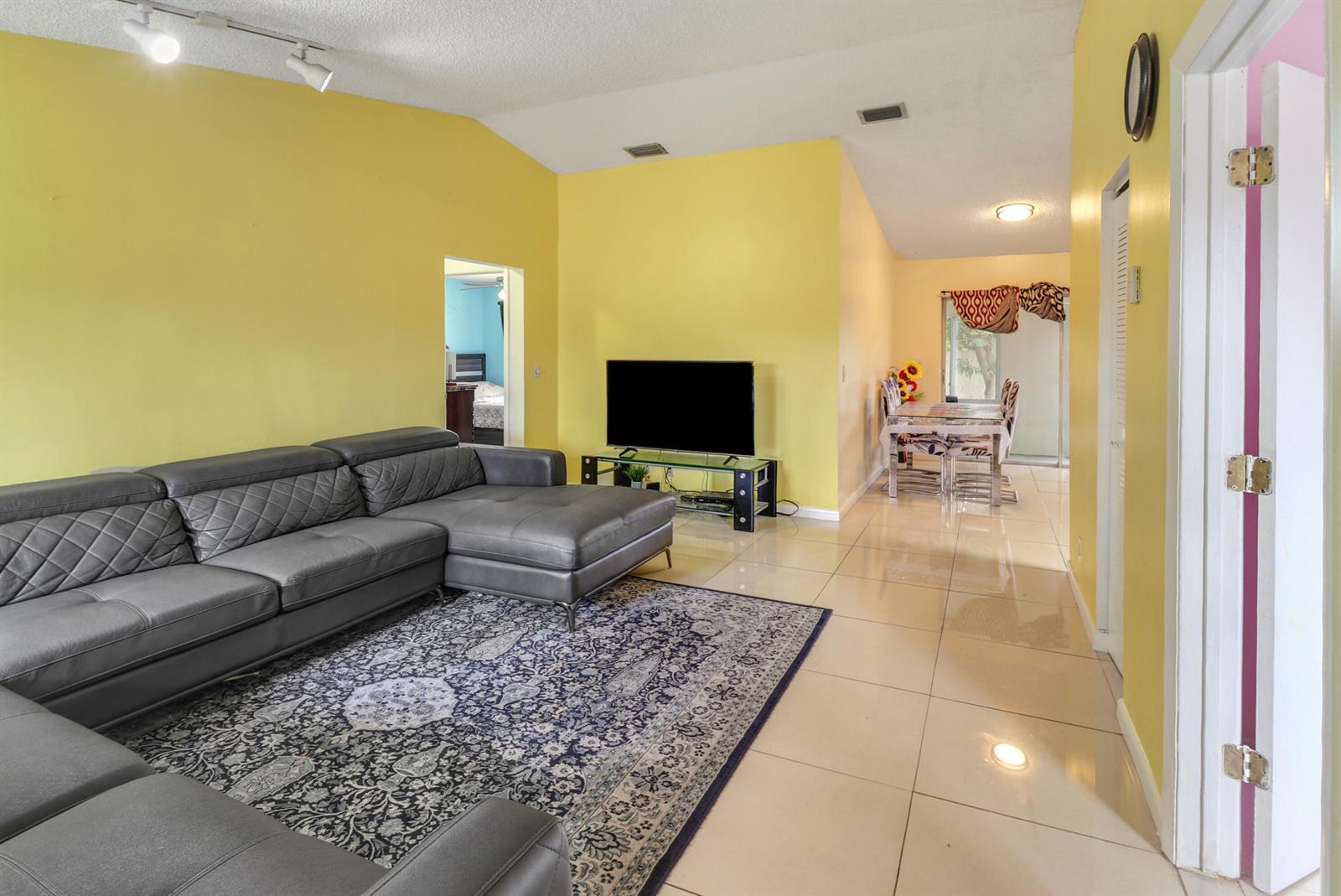 A living room with yellow walls, a grey sectional sofa, and tile flooring — 23 Chelsea Lane, Boynton Beach FL 33426, BOYNTON BEACH, FL