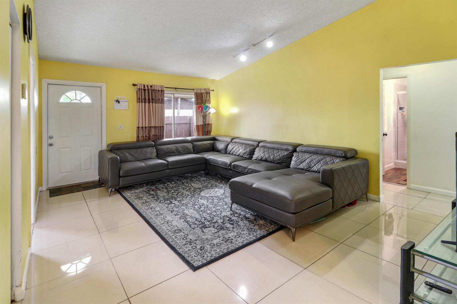 A living room features yellow walls, a large gray sectional sofa, and tiled flooring — 23 Chelsea Lane, Boynton Beach FL 33426, BOYNTON BEACH, FL