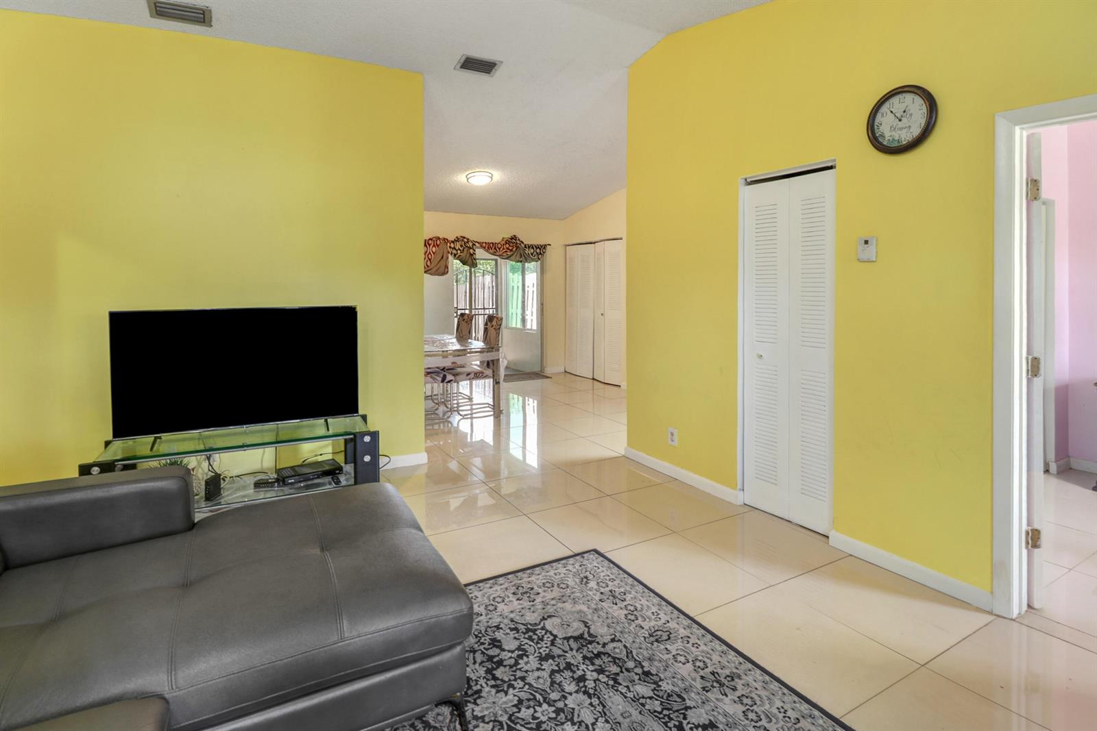 A living room with yellow walls, tile flooring, a gray sofa, and a television stand — 23 Chelsea Lane, Boynton Beach FL 33426, BOYNTON BEACH, FL