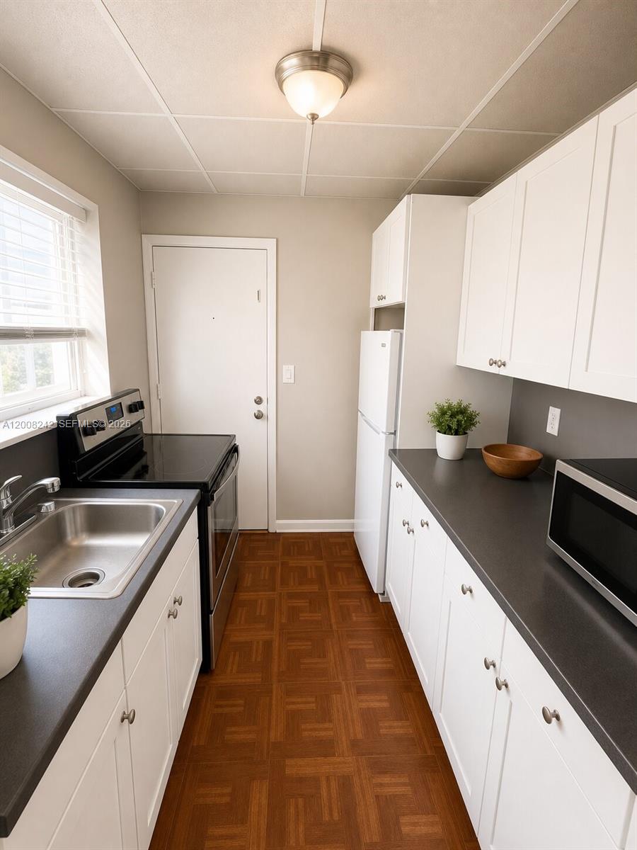 A galley kitchen features white cabinets, dark countertops, and wood-patterned flooring — 375 SW 19th Ave # 2, Miami FL 33135, MIAMI, FL