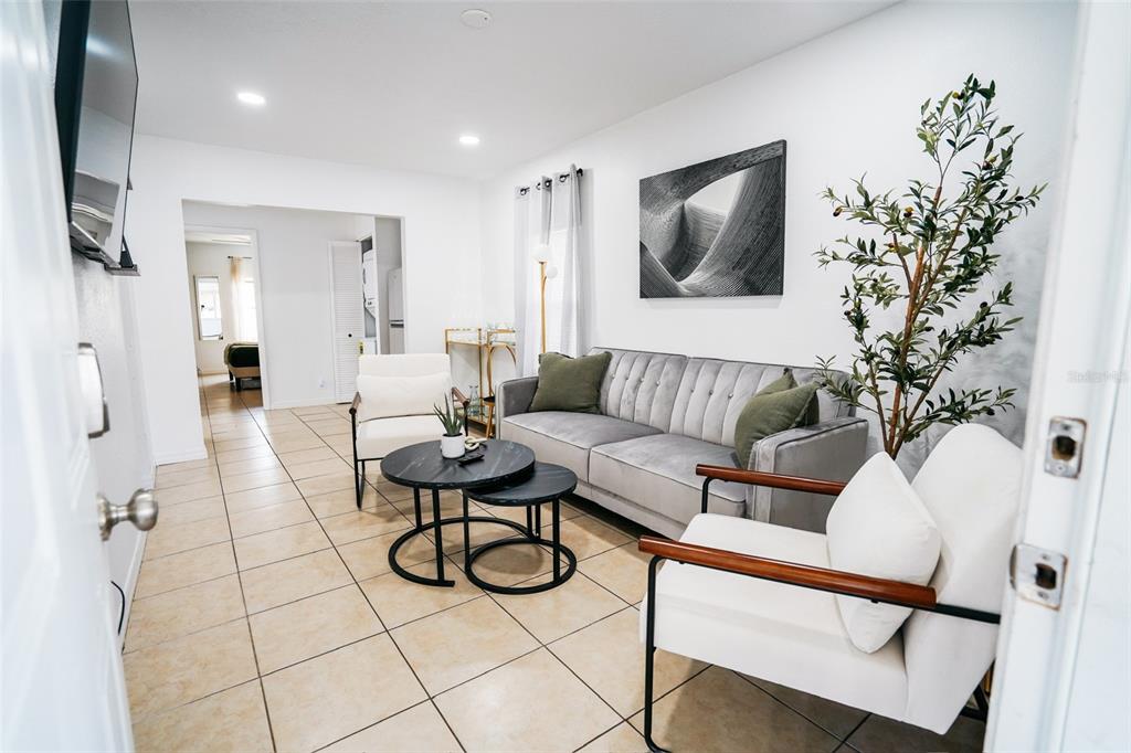 A living room features a gray tufted sofa, two white armchairs, and tiled flooring — 1361 29TH STREET S, ST PETERSBURG, FL