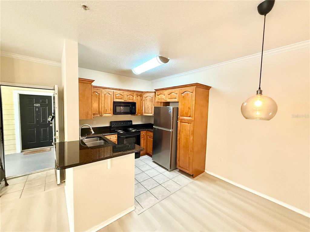 A kitchen features wood cabinets, stainless steel appliances, a granite countertop, and tile flooring — 2528 ROBERT TRENT JONES DRIVE UNIT 1625, ORLANDO, FL