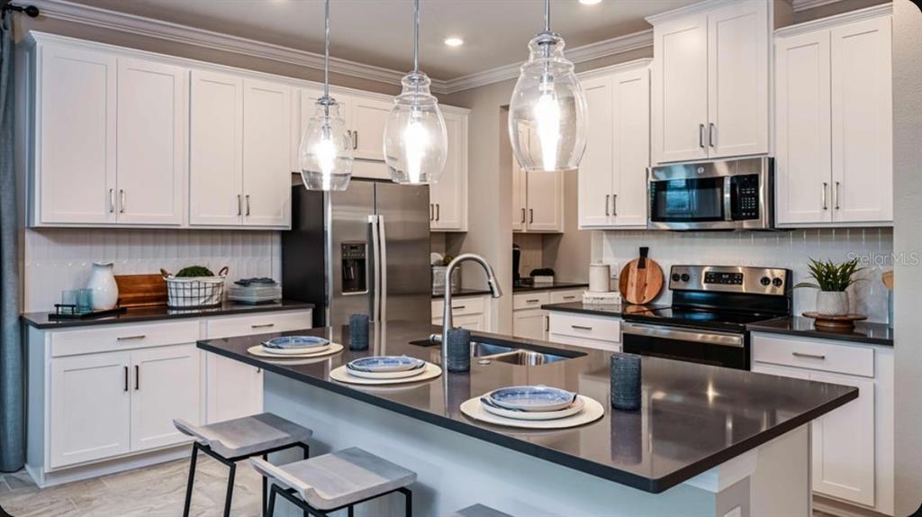 A kitchen with white cabinets, dark countertops, a center island, and three glass pendant lights — 7045 FOXBORO WAY, NOKOMIS, FL