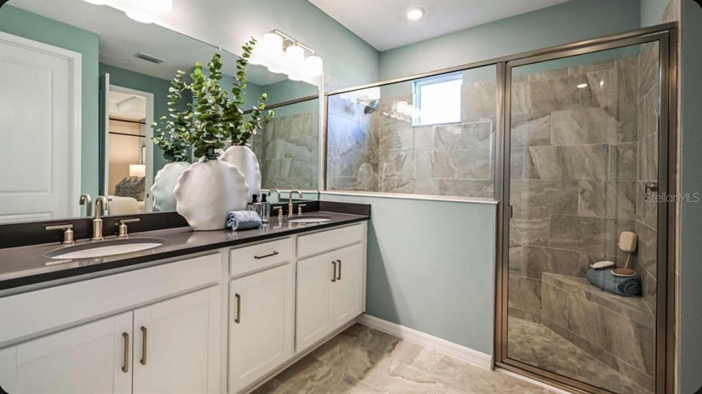 A bathroom features a double vanity with white cabinets, dark countertops, and a tiled shower — 7045 FOXBORO WAY, NOKOMIS, FL