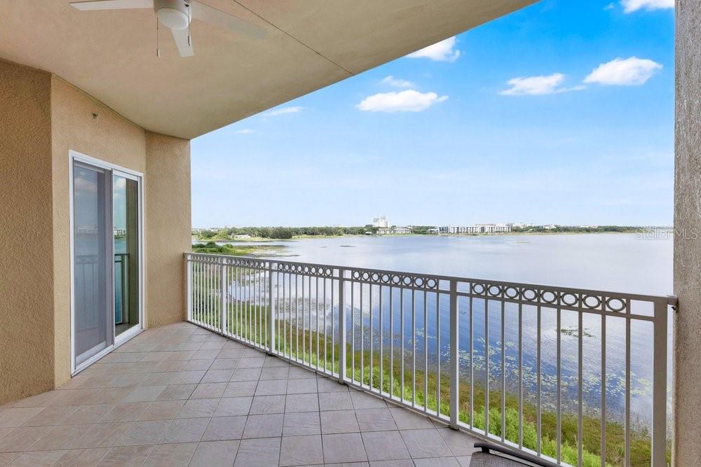 A covered balcony features tiled flooring, a white railing, and a view of a lake — 8749 THE ESPLANADE UNIT 22, ORLANDO, FL