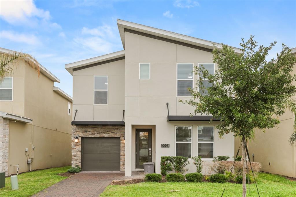 A two-story modern house with a stone-accented garage, a paved driveway, and a small lawn — 9093 SOMMERSET HILLS DRIVE, DAVENPORT, FL