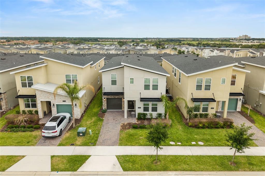 An aerial view shows three modern two-story suburban homes with paved driveways and green lawns — 9093 SOMMERSET HILLS DRIVE, DAVENPORT, FL