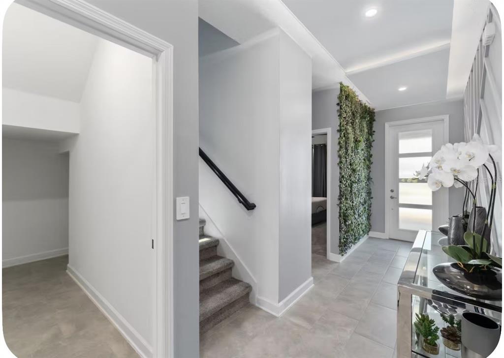 A bright entryway features gray tile flooring, a staircase with a black railing, and a green wall — 9093 SOMMERSET HILLS DRIVE, DAVENPORT, FL