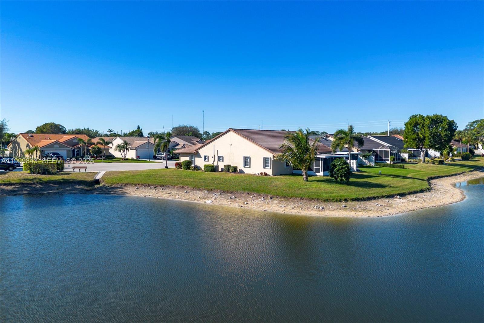 An aerial view shows a tan house with a tiled roof situated beside a lake — 4024 Summer Chase Ct, Lake Worth FL 33467, LAKE WORTH, FL