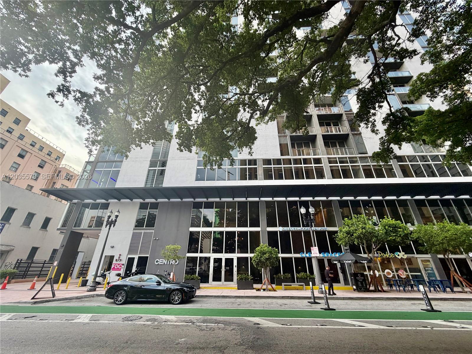 A multi-story building with a glass facade, ground-floor retail, and a black car parked outside — 151 SE 1st St # 408, Miami FL 33131, MIAMI, FL