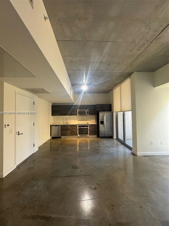 An open-concept kitchen features dark cabinetry, stainless steel appliances, and polished concrete floors — 151 SE 1st St # 408, Miami FL 33131, MIAMI, FL