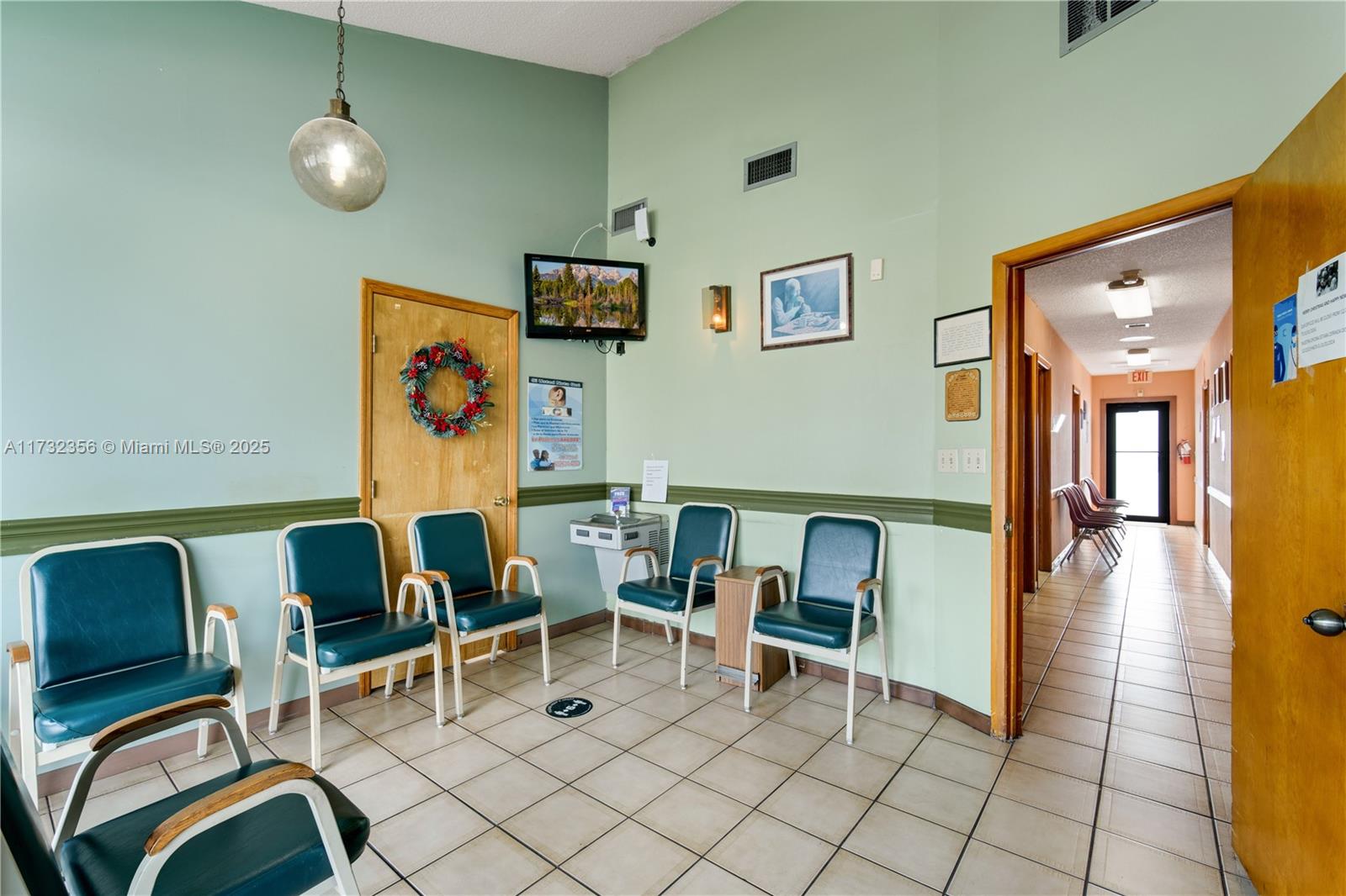 A waiting room features teal chairs, tile flooring, a water fountain, and a hallway entrance — 9950 SW 40th St, Miami FL 33165, MIAMI, FL