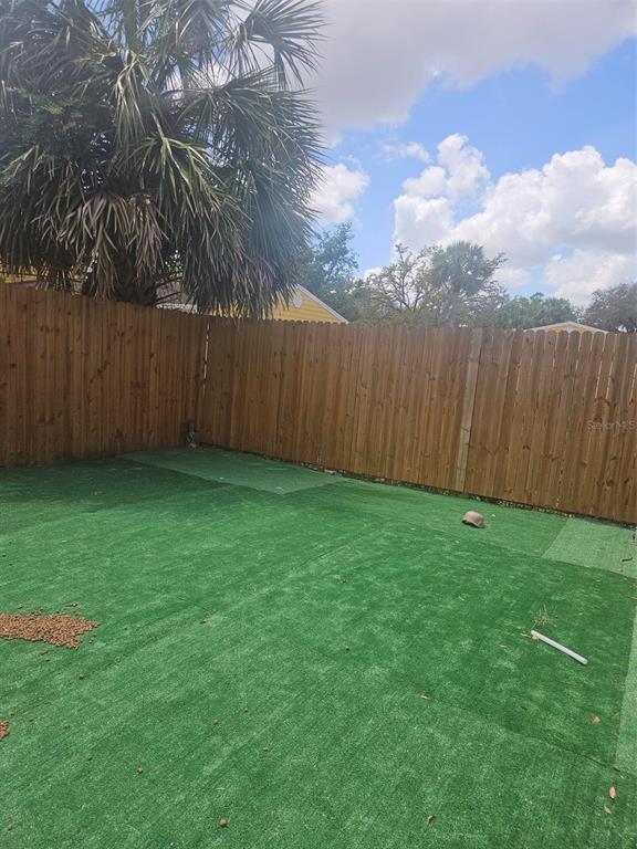 A fenced backyard features artificial turf, a palm tree, and a clear blue sky — 5134 TENNIS COURT CIRCLE, TAMPA, FL