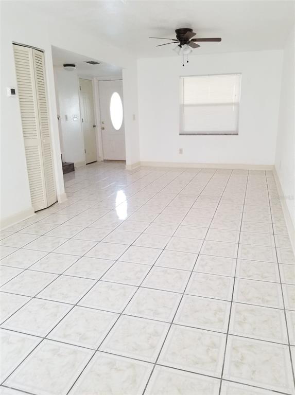 An empty room with white tiled floors, a ceiling fan, and a white front door — 5134 TENNIS COURT CIRCLE, TAMPA, FL