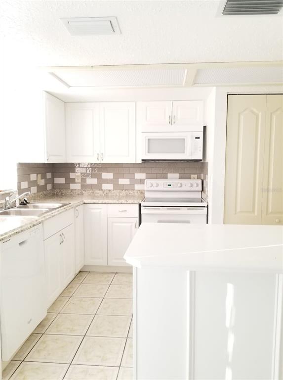 A kitchen with white cabinets, light countertops, a tiled backsplash, and white appliances — 5134 TENNIS COURT CIRCLE, TAMPA, FL