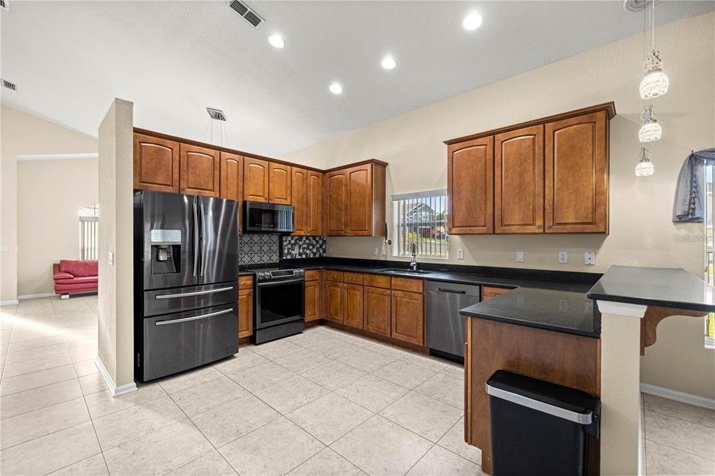 A kitchen with wood cabinets, black countertops, stainless steel appliances, and light tile flooring — 5438 SW 49TH AVENUE, OCALA, FL