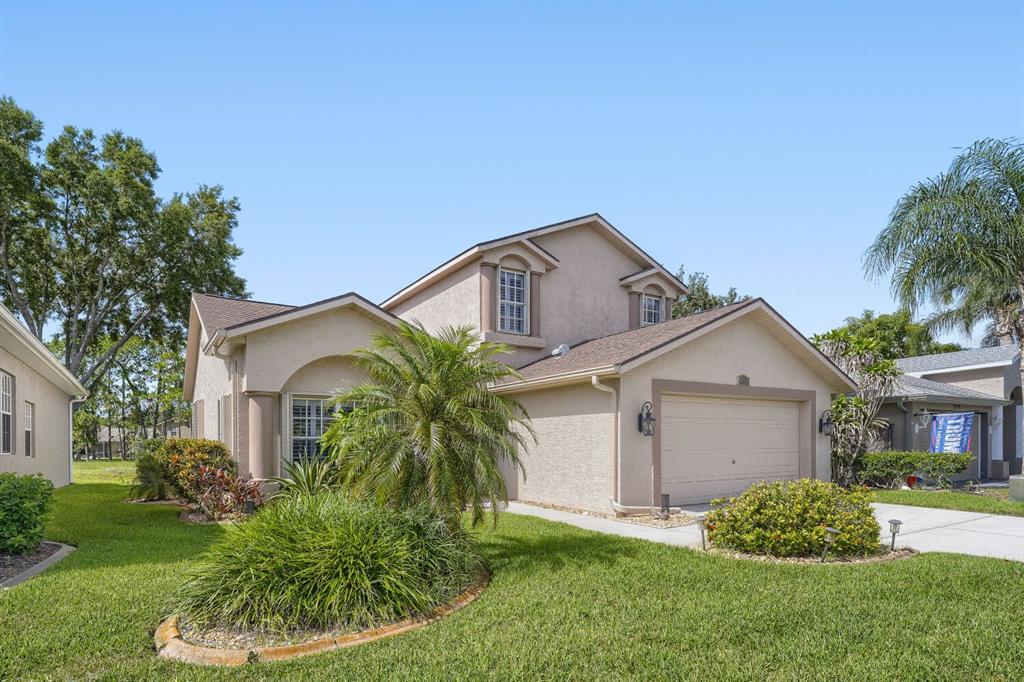 A two-story suburban house with a beige stucco exterior, a two-car garage, and landscaping — 11330 TEE TIME CIRCLE, NEW PORT RICHEY, FL