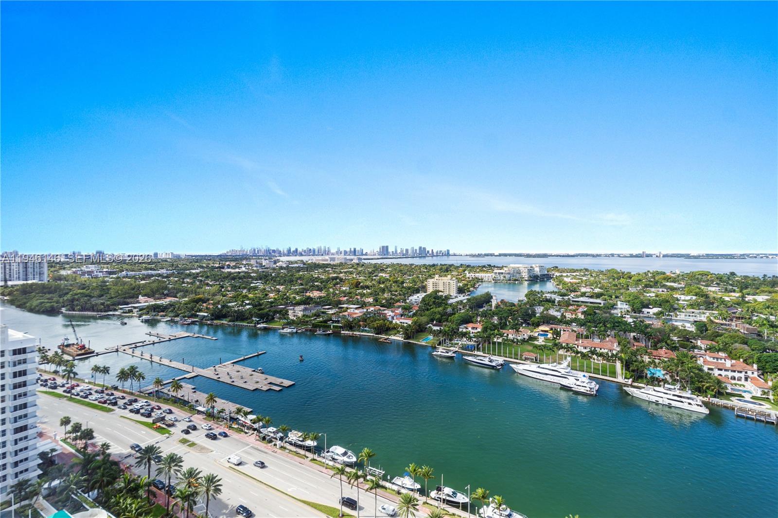 An aerial view shows a waterway with docked yachts, a coastal road, and distant city skyline — 4779 Collins Ave # 2607, Miami Beach FL 33140, MIAMI BEACH, FL