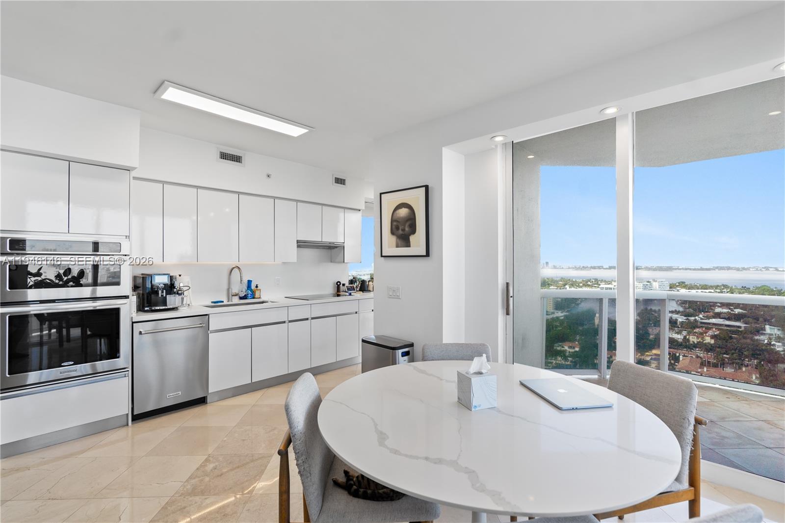 A modern kitchen with white cabinetry and a dining area overlooks a coastal cityscape — 4779 Collins Ave # 2607, Miami Beach FL 33140, MIAMI BEACH, FL