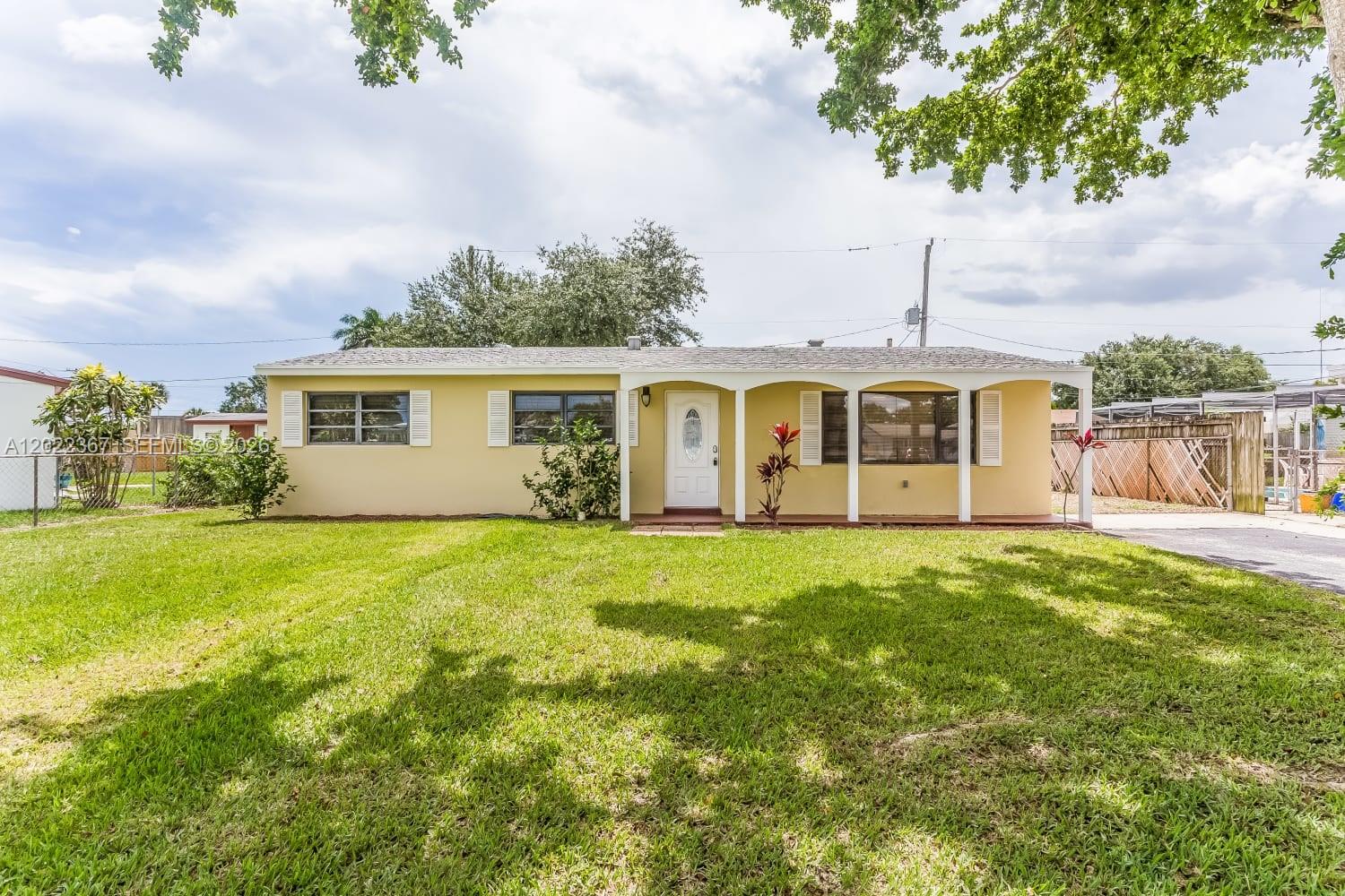 A single-story yellow house with a covered front porch and a large grassy yard — PALM BEACH GARDENS, FL