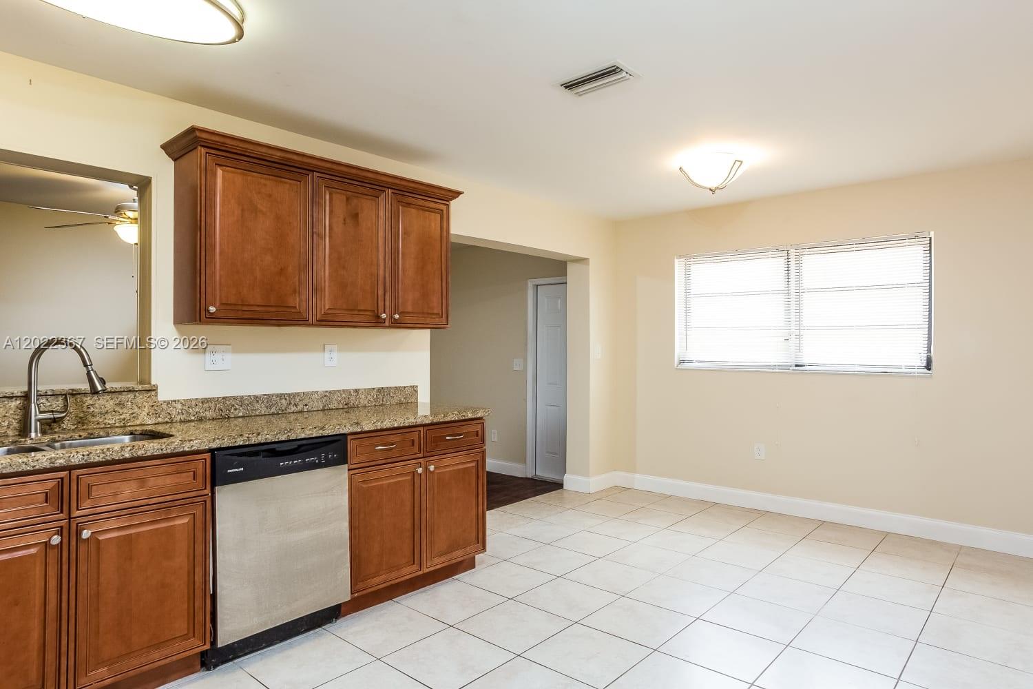 A kitchen features wood cabinets, granite countertops, a stainless steel dishwasher, and tile flooring — PALM BEACH GARDENS, FL