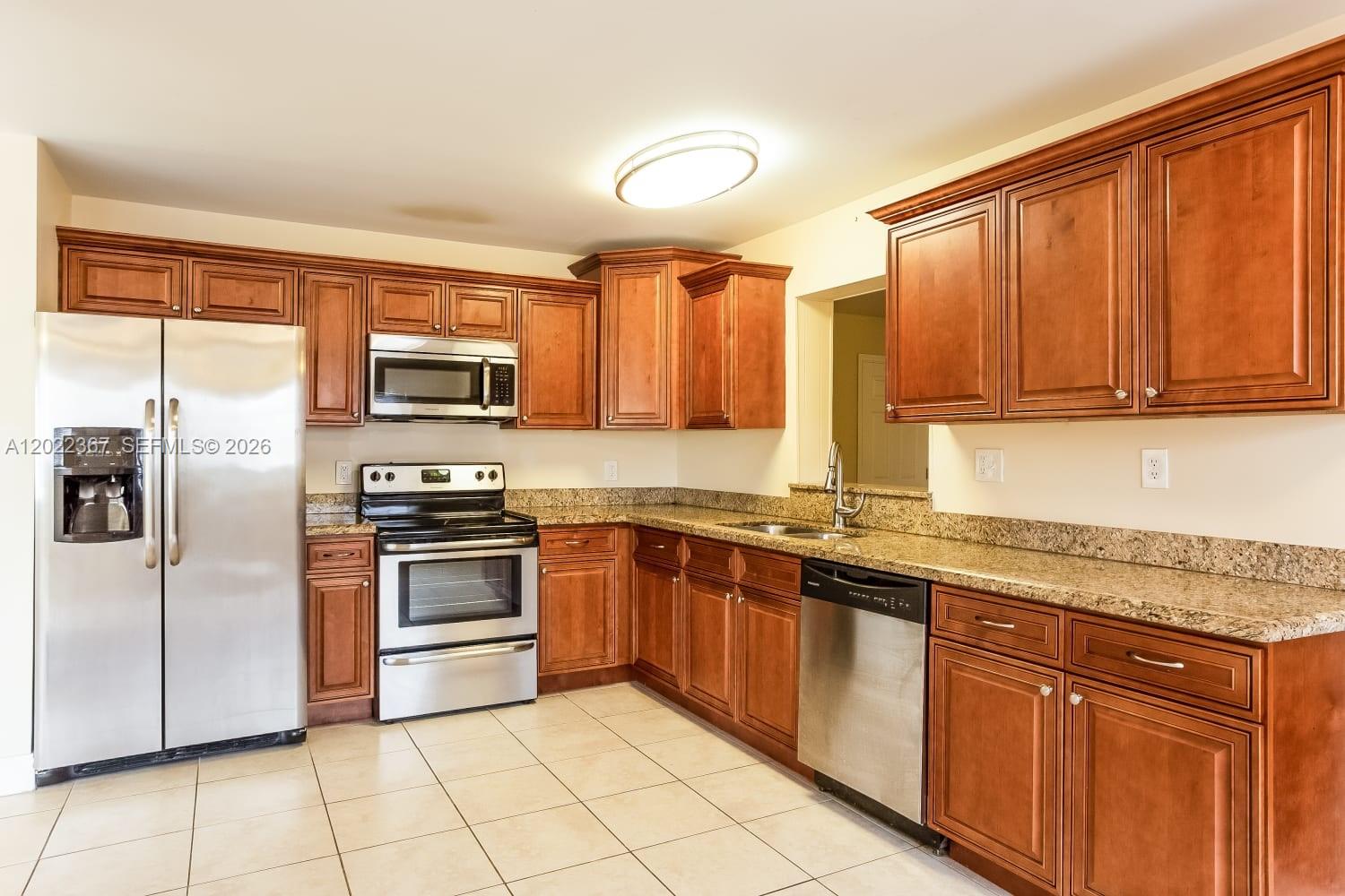 A kitchen features wood cabinets, granite countertops, stainless steel appliances, and tile flooring — PALM BEACH GARDENS, FL