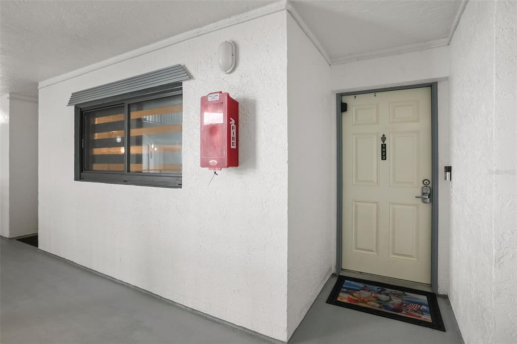 A white exterior wall features a window, a red fire extinguisher cabinet, and a door — 5207 S ATLANTIC AVENUE UNIT 1023, NEW SMYRNA BEACH, FL