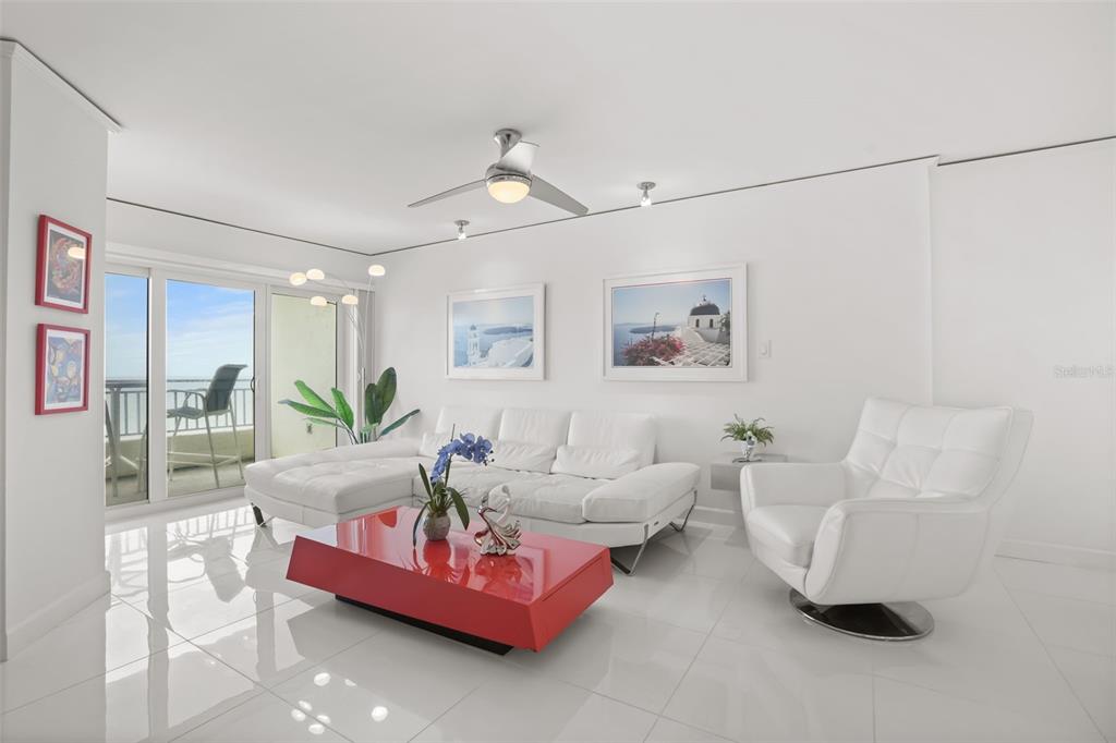 A bright living room features white furniture, a red coffee table, and a balcony view — 5207 S ATLANTIC AVENUE UNIT 1023, NEW SMYRNA BEACH, FL