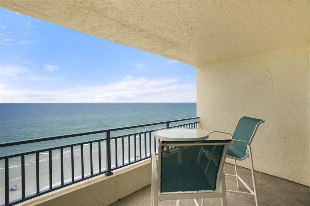 A balcony with a metal railing overlooks the ocean with a small table and chairs — 5207 S ATLANTIC AVENUE UNIT 1023, NEW SMYRNA BEACH, FL
