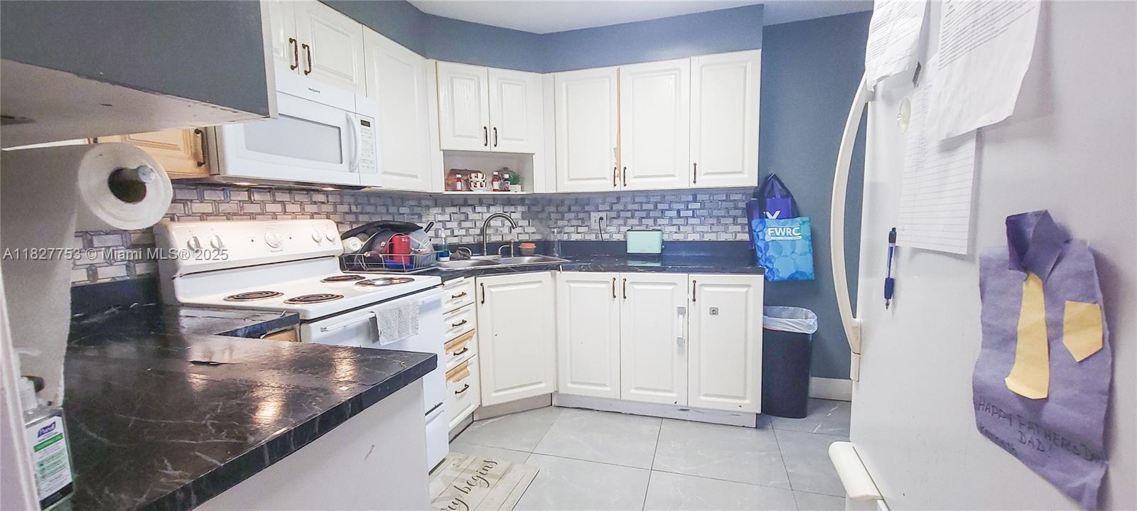 A kitchen features white cabinets, dark countertops, a white stove, and a blue-gray wall — 3301 Spanish Moss Ter # 609, Lauderhill FL 33319, LAUDERHILL, FL