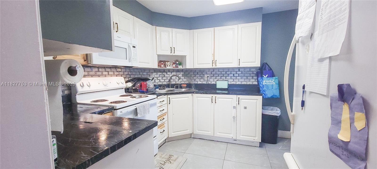 A kitchen features white cabinets, dark countertops, a tiled backsplash, and light-colored floor tiles — 3301 Spanish Moss Ter # 609, Lauderhill FL 33319, LAUDERHILL, FL