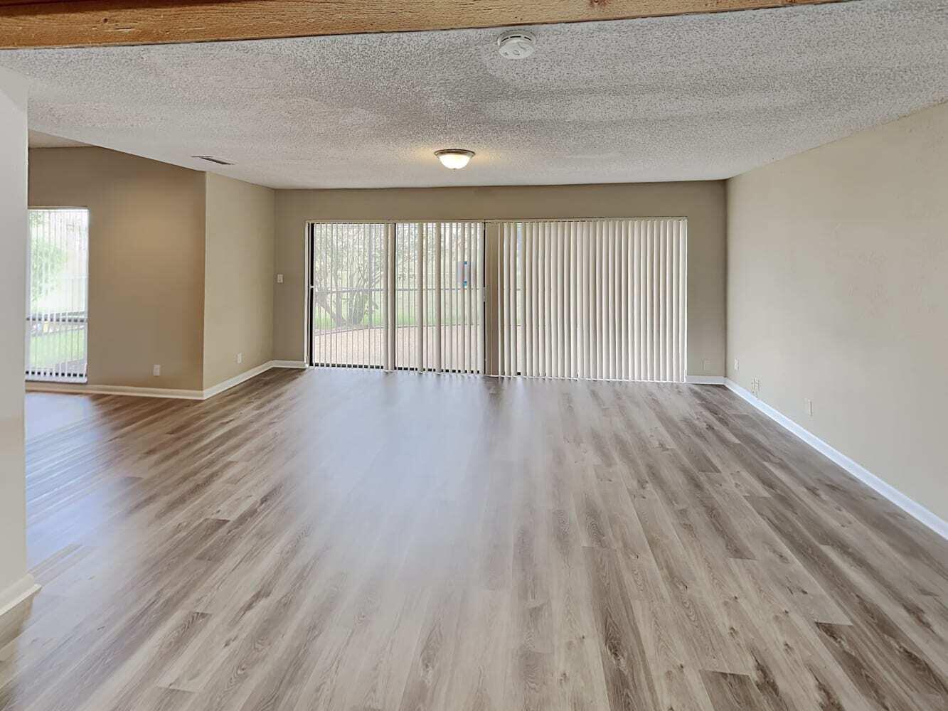 An empty living room features light wood-look flooring, beige walls, and large sliding glass doors — TAMARAC, FL