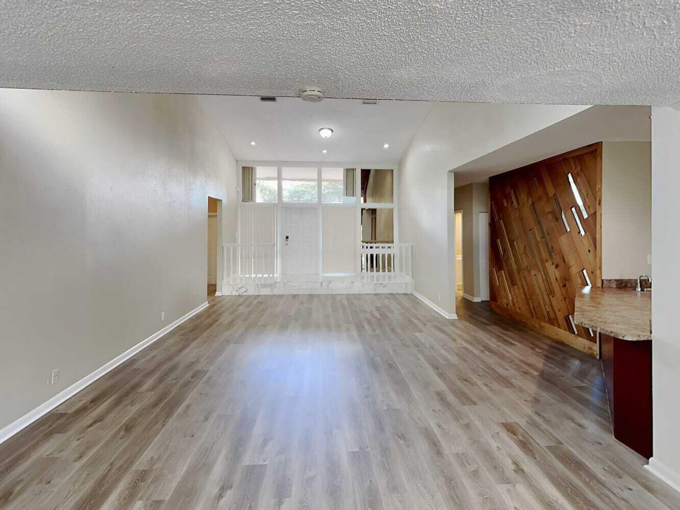 A spacious living room features light wood-look flooring, a raised entryway, and a wood-paneled wall — TAMARAC, FL