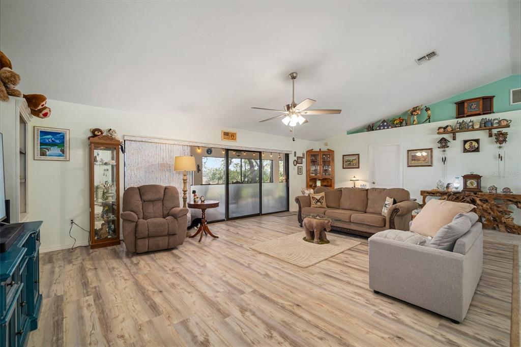 A living room features light wood-look flooring, a vaulted ceiling, and a sliding glass door — 1472 IVYDALE ROAD, SPRING HILL, FL