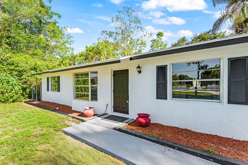 The exterior of a white, single-story house features a dark front door and shutters — 11852 N 47th Rd Road N, FL 33411, FL