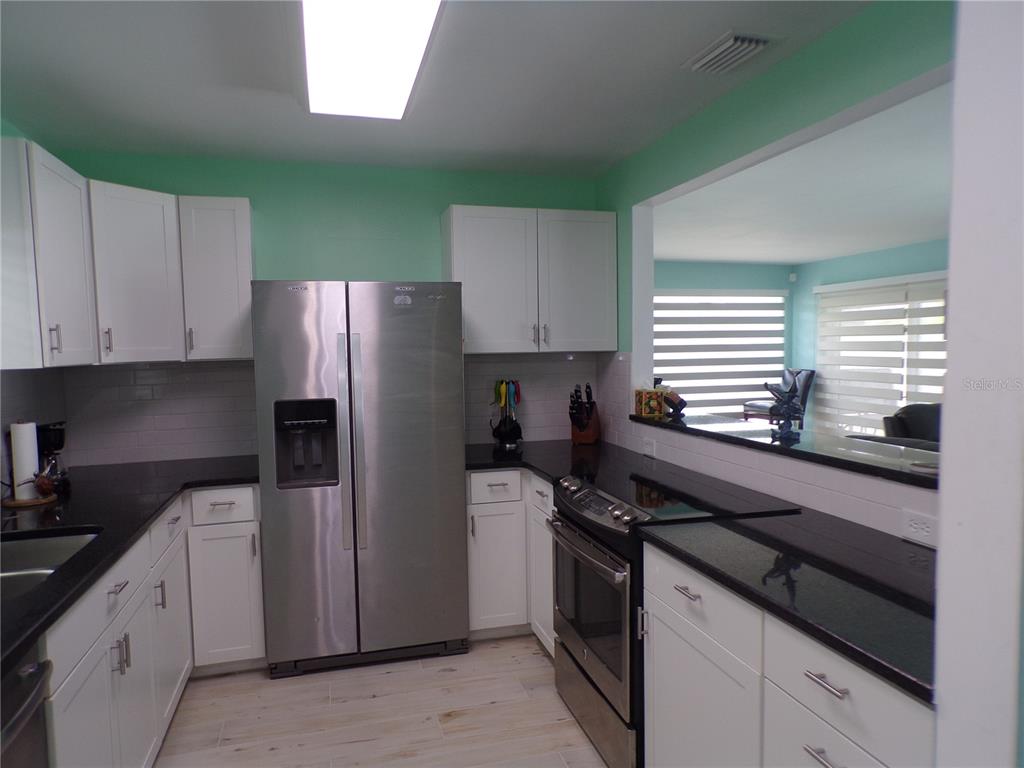 A kitchen features white cabinets, black countertops, stainless steel appliances, and light-colored wood-look flooring — 21088 EDGEWATER DRIVE, PORT CHARLOTTE, FL