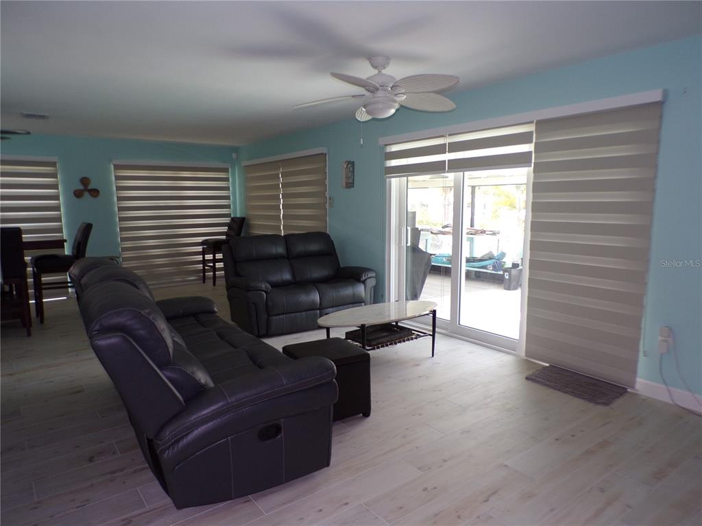 A living room features light blue walls, wood-look tile flooring, black leather furniture, and sliding doors — 21088 EDGEWATER DRIVE, PORT CHARLOTTE, FL