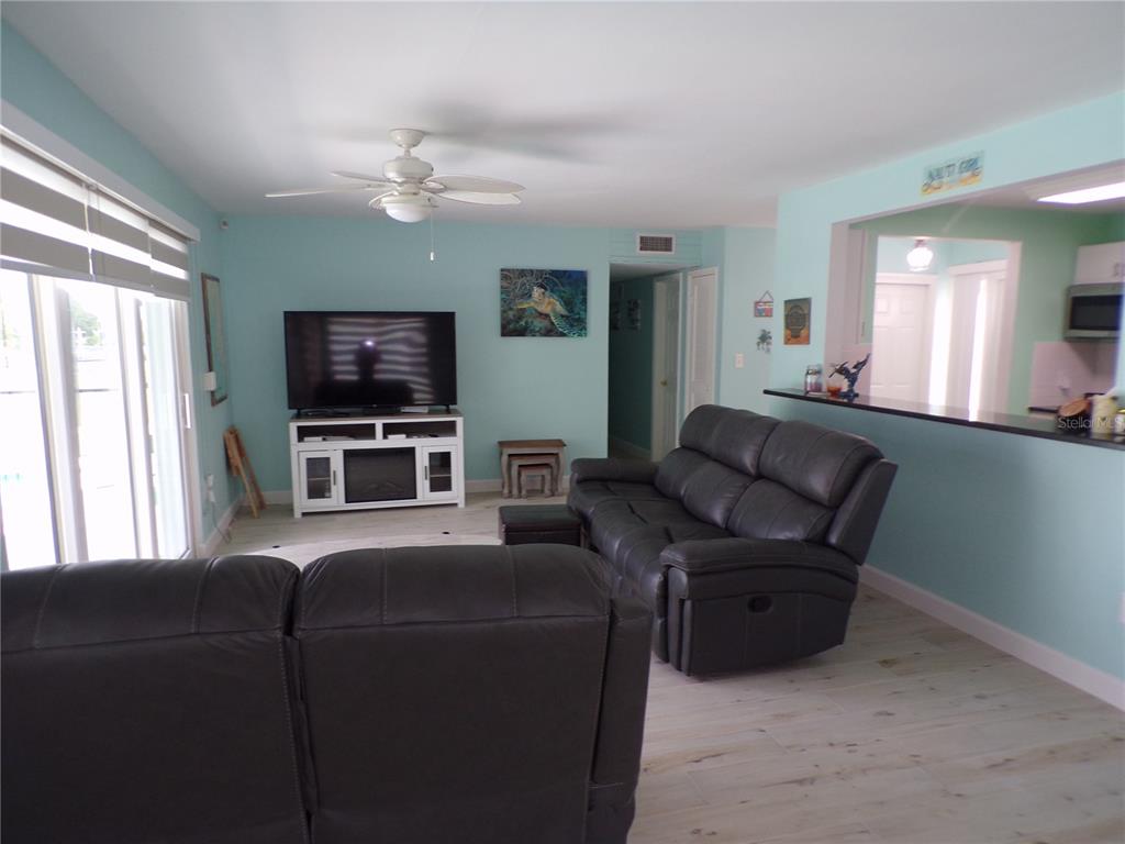 A living room with light blue walls, wood-look flooring, two dark leather sofas, and a television — 21088 EDGEWATER DRIVE, PORT CHARLOTTE, FL