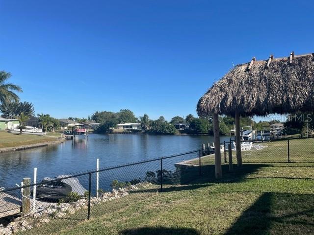 A thatched-roof tiki hut stands near a chain-link fence overlooking a canal with boats — 21088 EDGEWATER DRIVE, PORT CHARLOTTE, FL