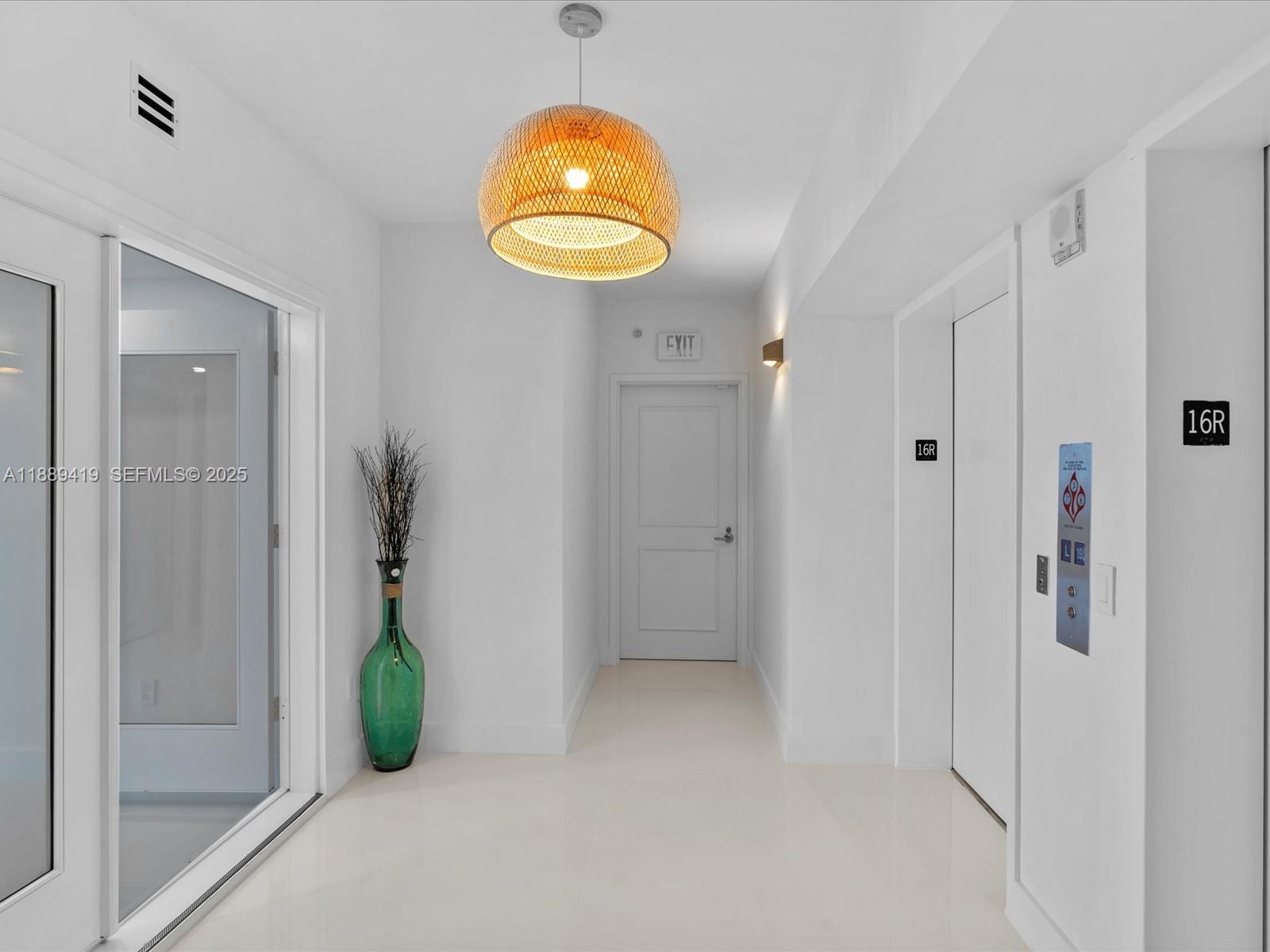 A bright hallway features white walls, a woven pendant light, an elevator, and an exit door — 3101 S Ocean Dr # 1608, Hollywood FL 33019, HOLLYWOOD, FL