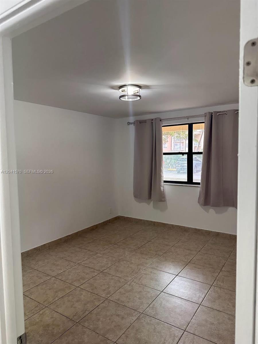 An empty room features beige tile flooring, white walls, a ceiling light, and window curtains — 8100 Geneva Ct # 142, Doral FL 33166, DORAL, FL