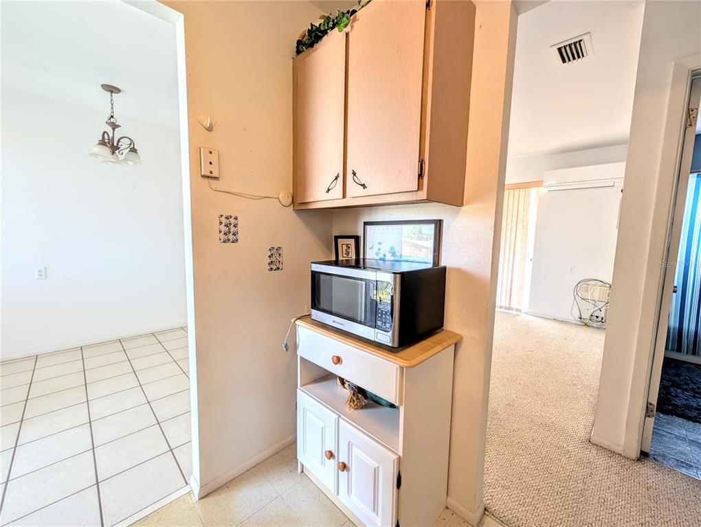 A microwave sits on a white cabinet beneath a wooden wall cabinet in a hallway — 5951 TODD STREET UNIT D37, BRADENTON, FL