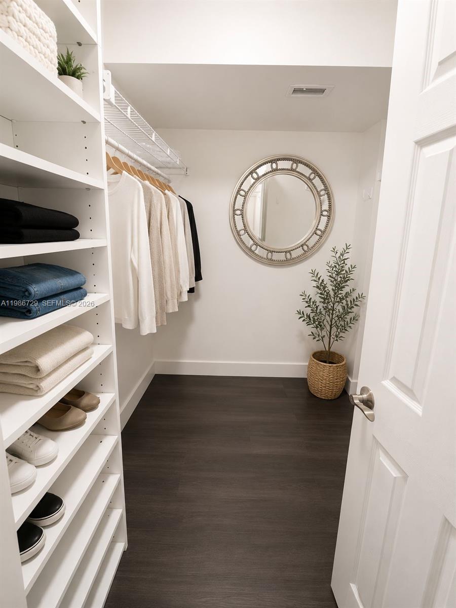 A walk-in closet features white shelving, hanging clothes, a round mirror, and dark flooring — 299 NW 52nd Ter # X, Boca Raton FL 33487, BOCA RATON, FL