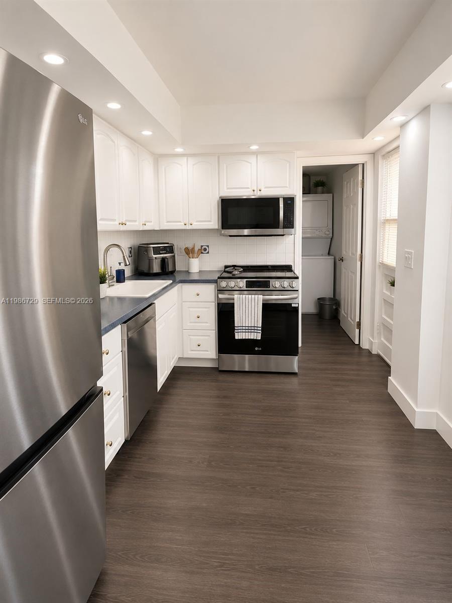 A galley-style kitchen features white cabinets, stainless steel appliances, and dark wood-look flooring — 299 NW 52nd Ter # X, Boca Raton FL 33487, BOCA RATON, FL
