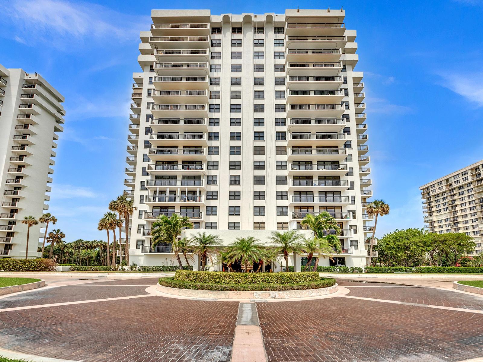 A tall, multi-story residential building with balconies stands behind a circular brick driveway — 2003 N Ocean Boulevard # 602, Boca Raton FL 33431, BOCA RATON, FL