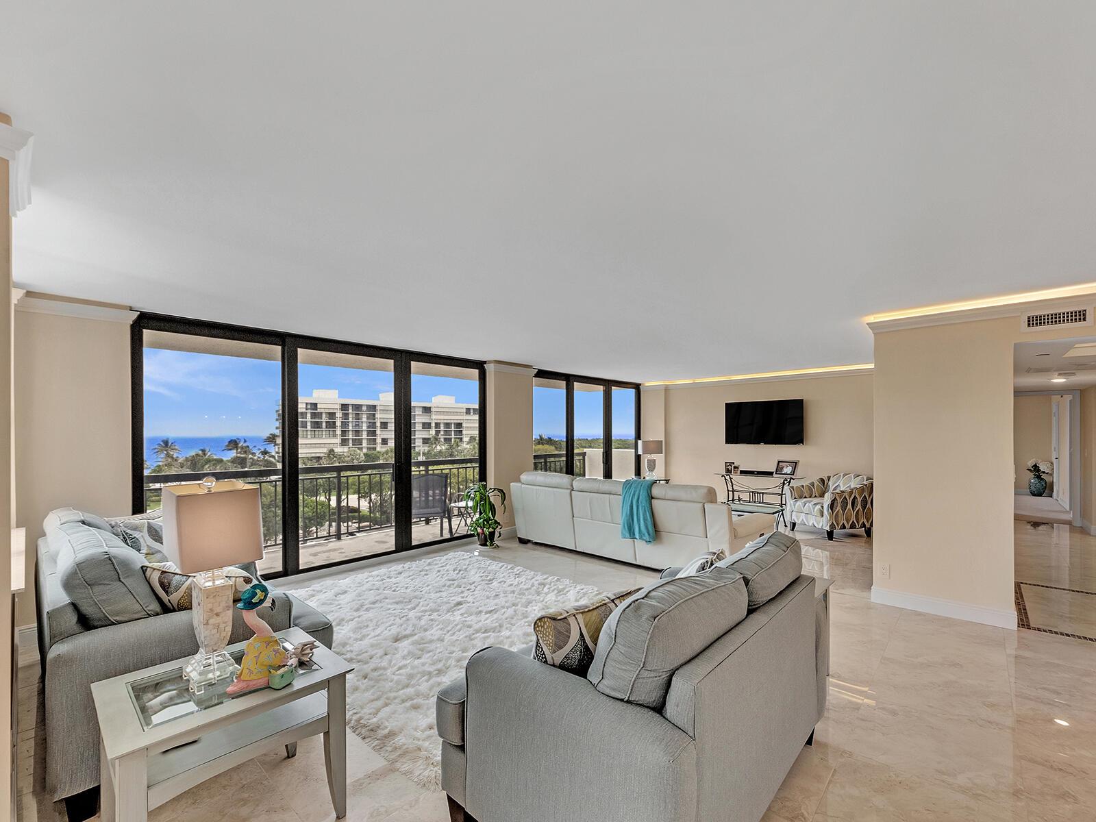 A living room with light gray sofas, a white rug, and floor-to-ceiling windows overlooking the ocean — 2003 N Ocean Boulevard # 602, Boca Raton FL 33431, BOCA RATON, FL