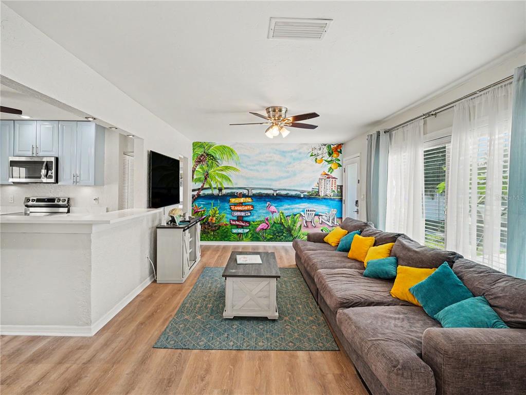 A living room features a large tropical mural, a gray sectional sofa, and light wood flooring — 2547 BAHIA VISTA STREET, SARASOTA, FL