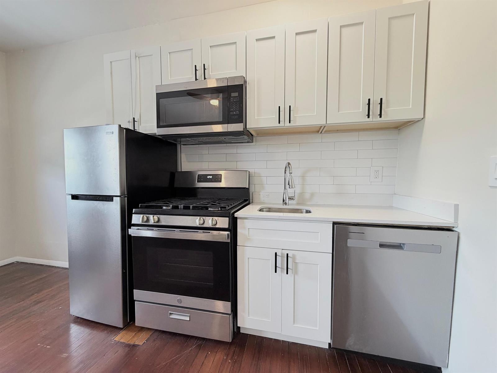 A kitchen features white cabinets, stainless steel appliances, a subway tile backsplash, and wood flooring — 623 Park Place Unit 5, West Palm Beach FL 33401, WEST PALM BEACH, FL