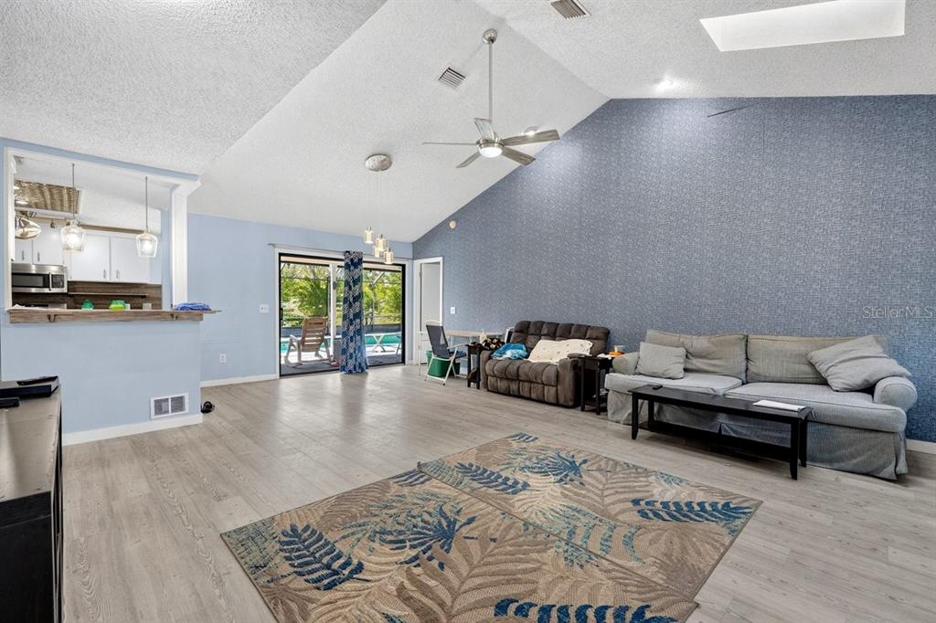 A living room with vaulted ceilings, a blue accent wall, and sliding glass doors to a pool — 19 BIG DIPPER LANE, PALM COAST, FL