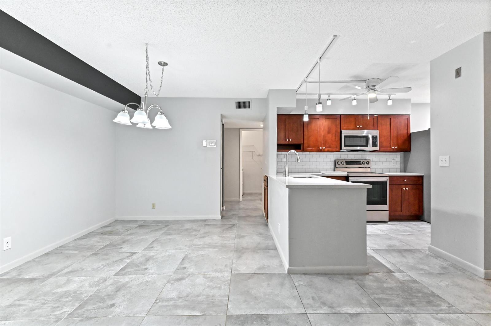 A kitchen features dark wood cabinets, stainless steel appliances, white countertops, and white subway tile — 14895 Builtmore Way # 107, Delray Beach FL 33446, DELRAY BEACH, FL